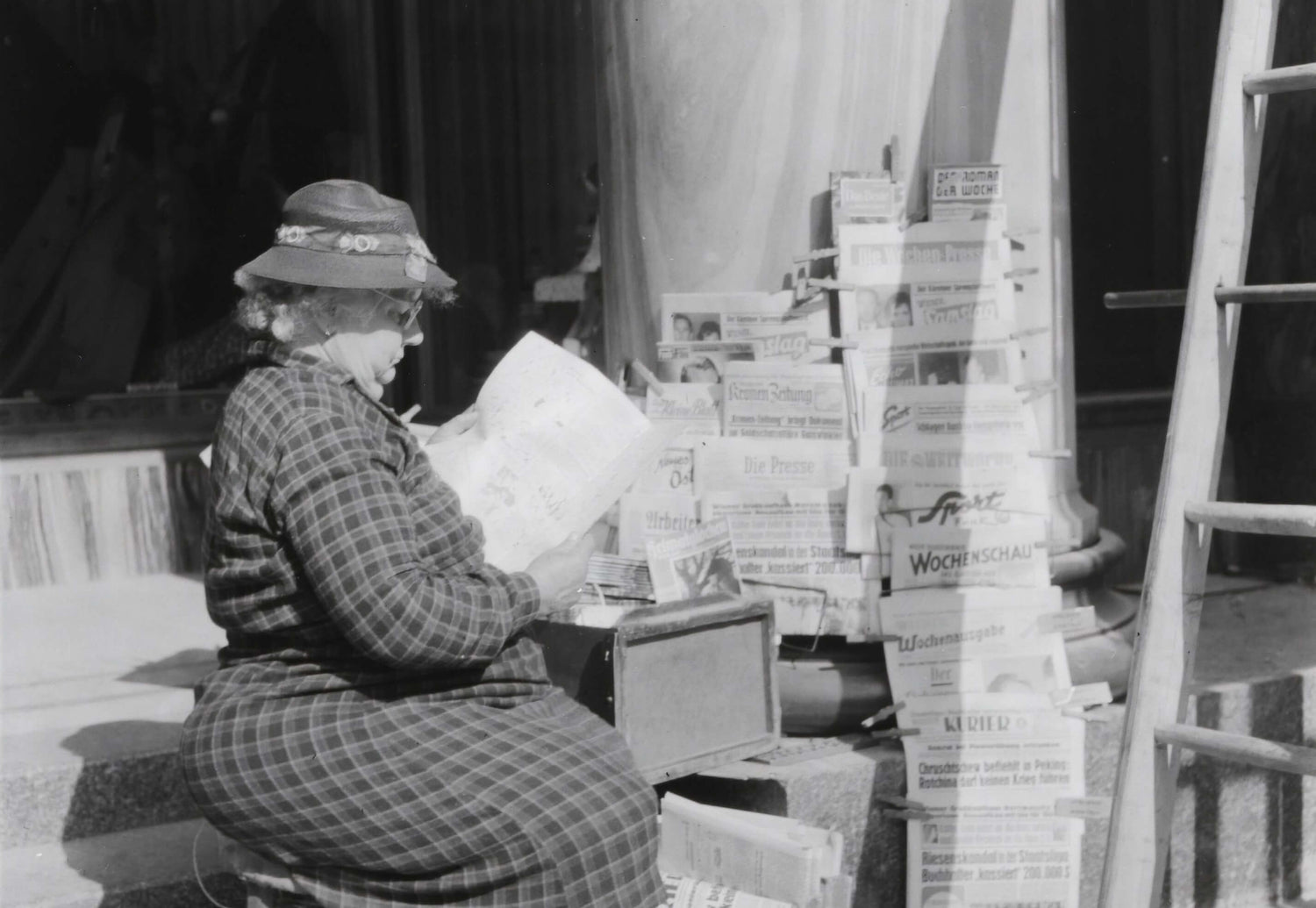 Dame sitzt auf einer Bank und liest das Tagesblatt. 