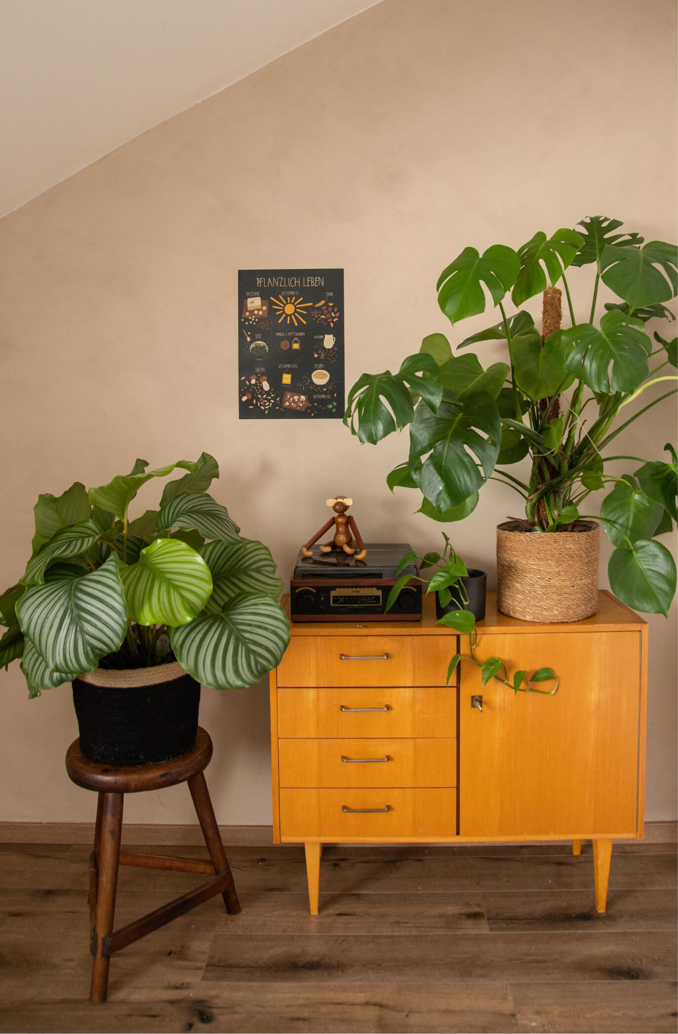 Das Pflanzlich leben Poster mit allen wichtigen veganen Nährstoffen hängt an der Wand, zwischendrin sind Vintage Möbel und Pflanzen.
